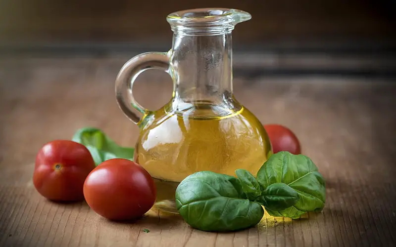 A bottle of olive oil, tomatoes and basil leaves